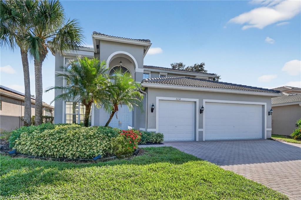 Mediterranean / spanish-style home featuring stucco siding, a tiled roof, decorative driveway, a front yard, and an attached garage