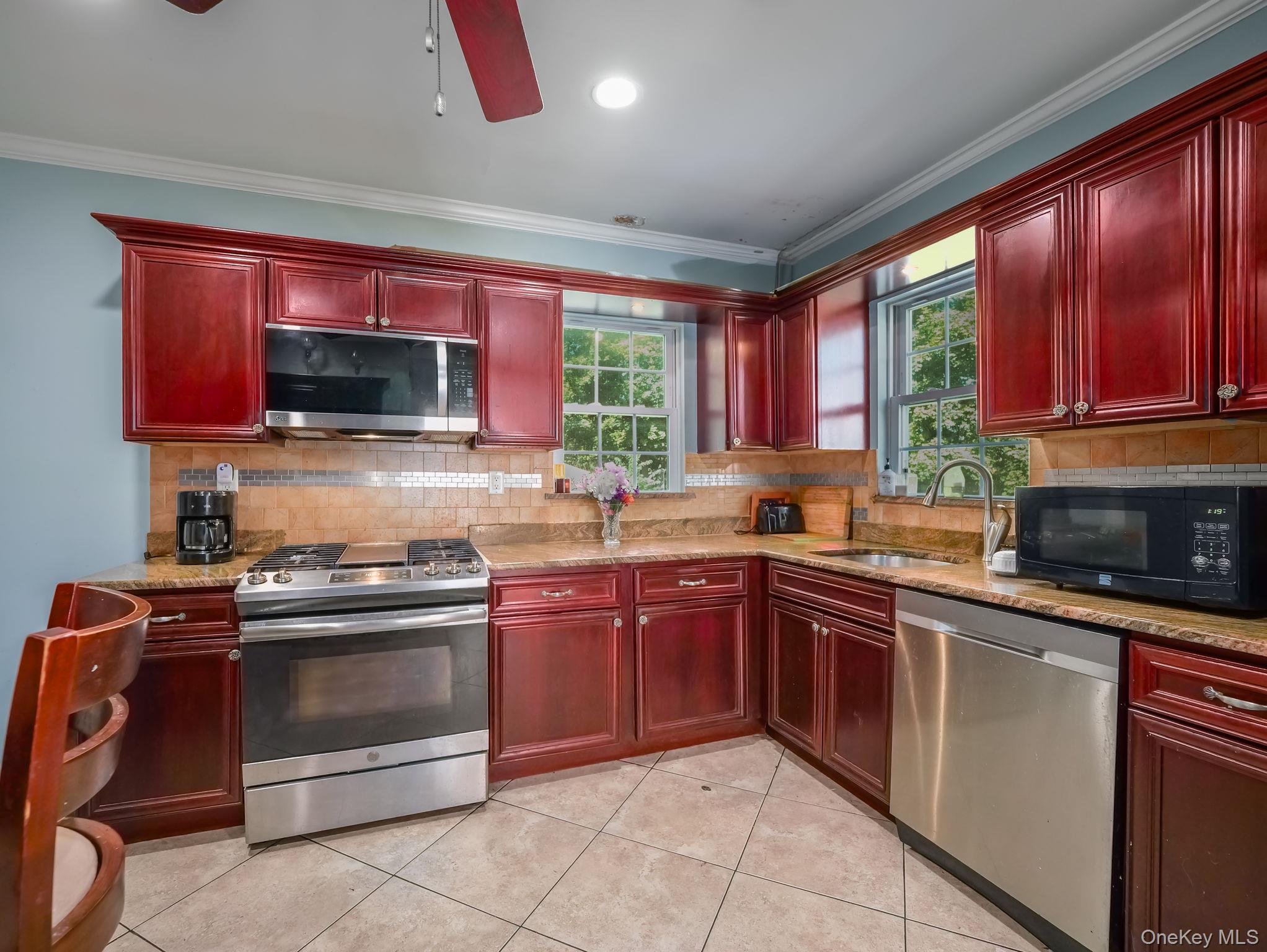 3 South Myrtle Avenue Spring Valley, NY 10977 - Photo 20 of 40 Kitchen with reddish brown cabinets, appliances with stainless steel finishes, light stone counters, decorative backsplash, and crown molding