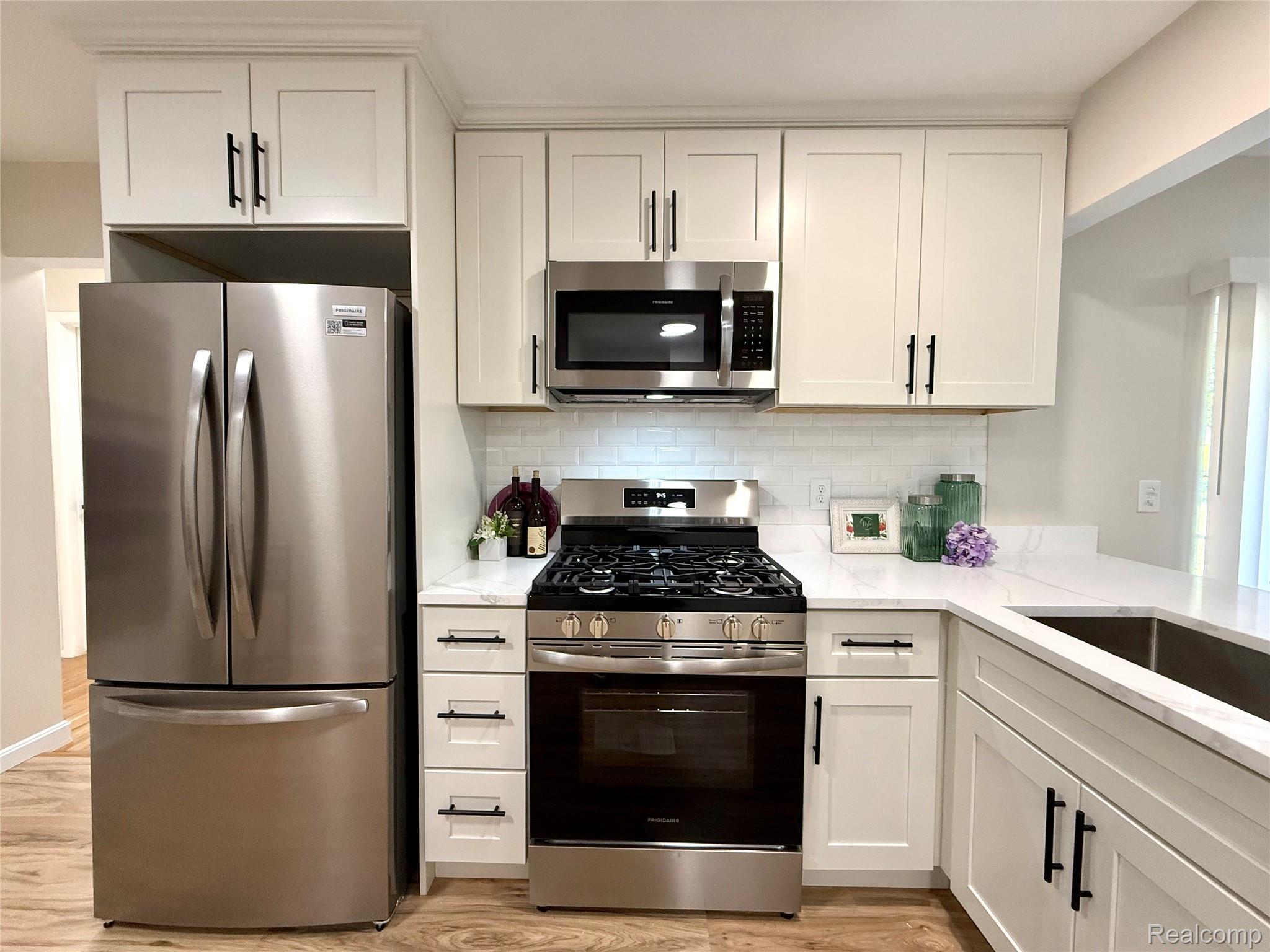 39909 Lynn Street Canton, MI 48187 - Photo 9 of 45 Modern kitchen featuring white shaker cabinetry, stainless steel appliances, a white subway tile backsplash, light-toned countertops, and wood-finish flooring