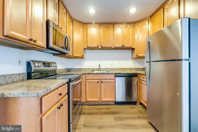 a kitchen with stainless steel appliances granite countertop a refrigerator a sink dishwasher a stove with wooden cabinets and floor