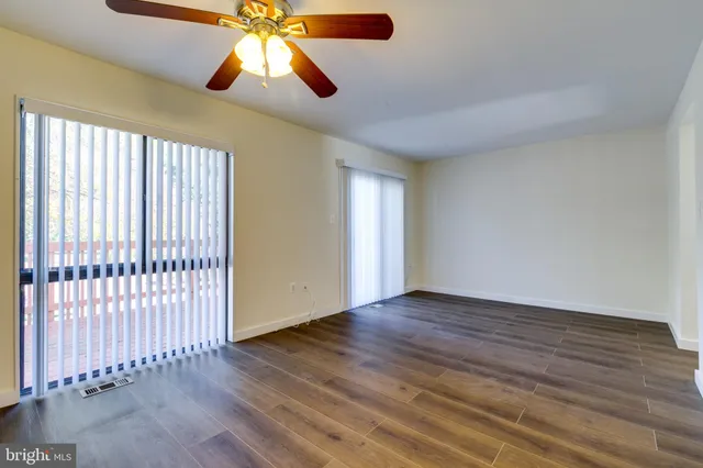 an empty room with wooden floor chandelier fan and windows