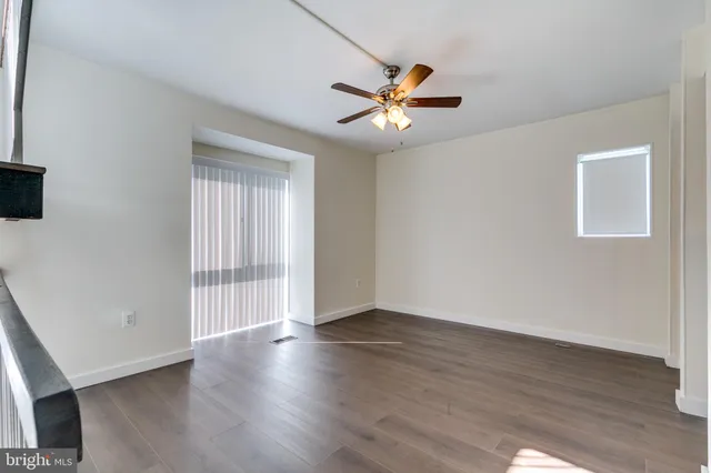 an empty room with wooden floor fan and windows
