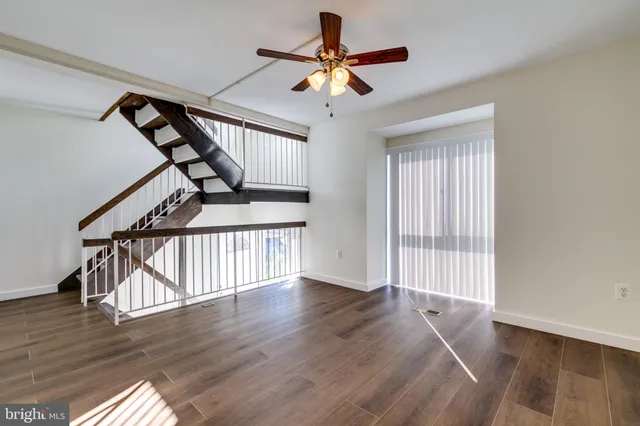 a view of an empty room with wooden floor and a ceiling fan