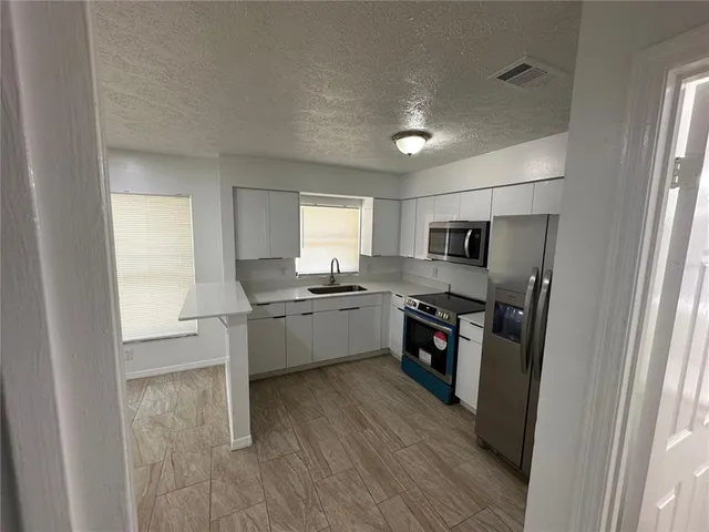 a kitchen with stainless steel appliances granite countertop a refrigerator a sink dishwasher a stove and white countertops with wooden floor