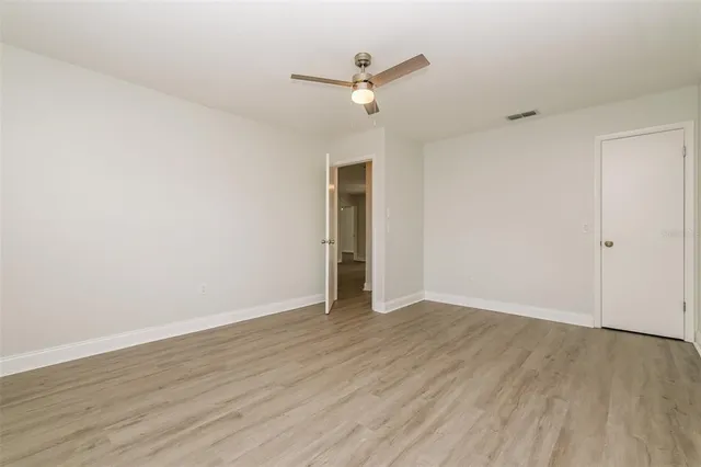 an empty room with wooden floor fan and windows