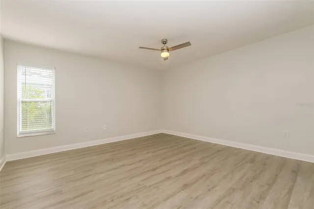 a view of an empty room with wooden floor and a ceiling fan