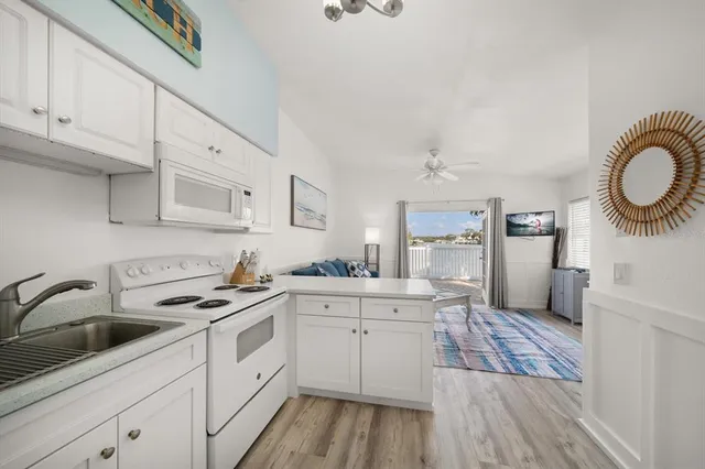 a kitchen with a sink dishwasher a stove and white cabinets with wooden floor