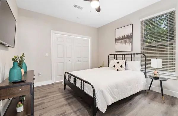 a bedroom with a bed a potted plant on dresser and a wooden floor
