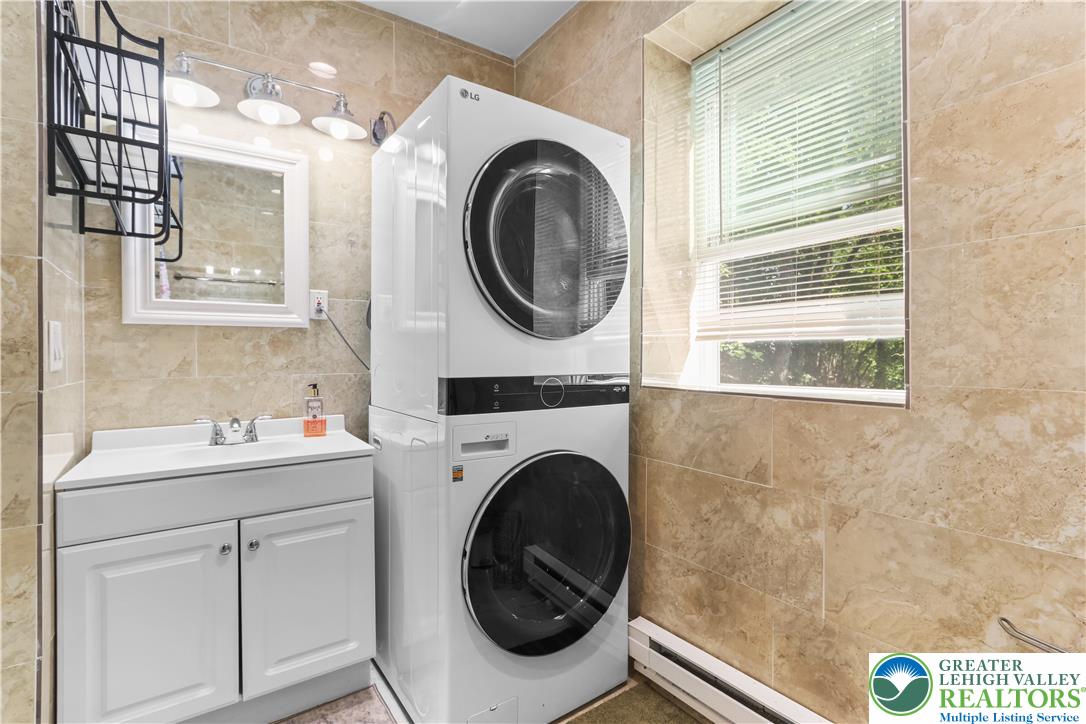 1007 Hampstead Road Bushkill, PA 18324 - Photo 40 of 72 A neatly arranged laundry area features a stackable washer and dryer, complemented by a convenient vanity sink and neutral tiled walls.