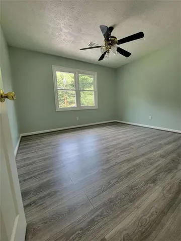 an empty room with wooden floor chandelier fan and windows
