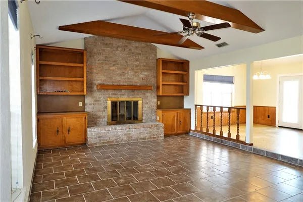 a view of a livingroom with a fireplace a ceiling fan and windows