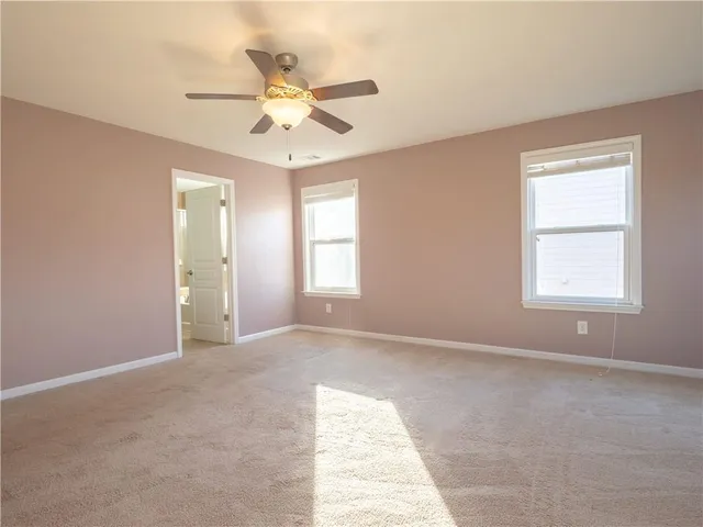 an empty room with ceiling fan and windows