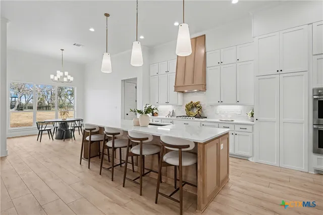 an open kitchen with granite countertop a stove a sink a dining table and chairs with wooden floor