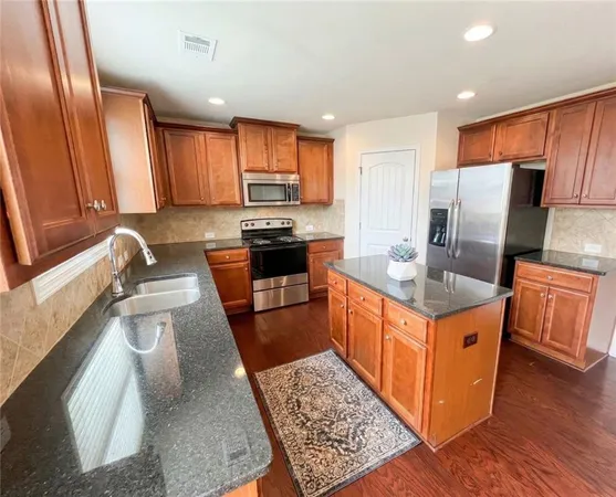 a kitchen with stainless steel appliances granite countertop a stove top oven a sink dishwasher a refrigerator and cabinets with wooden floor