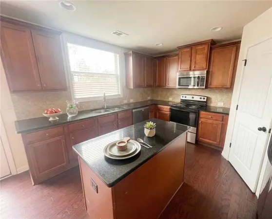 a kitchen with stainless steel appliances granite countertop a stove a refrigerator a sink a dining table and chairs with wooden floor