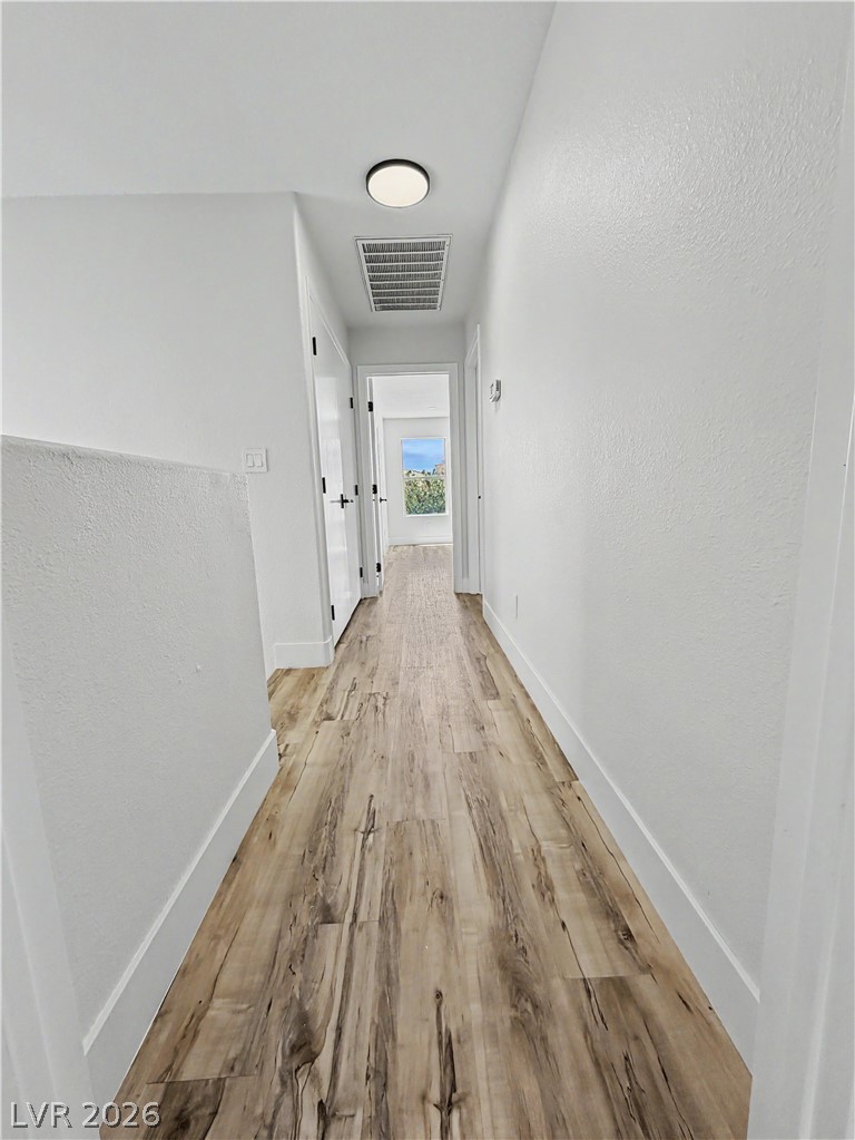 8977 Paige Rene Court Las Vegas, NV 89117 - Photo 29 of 31 A well-lit corridor with warm-toned wood flooring leads toward a sun-drenched window at its end.