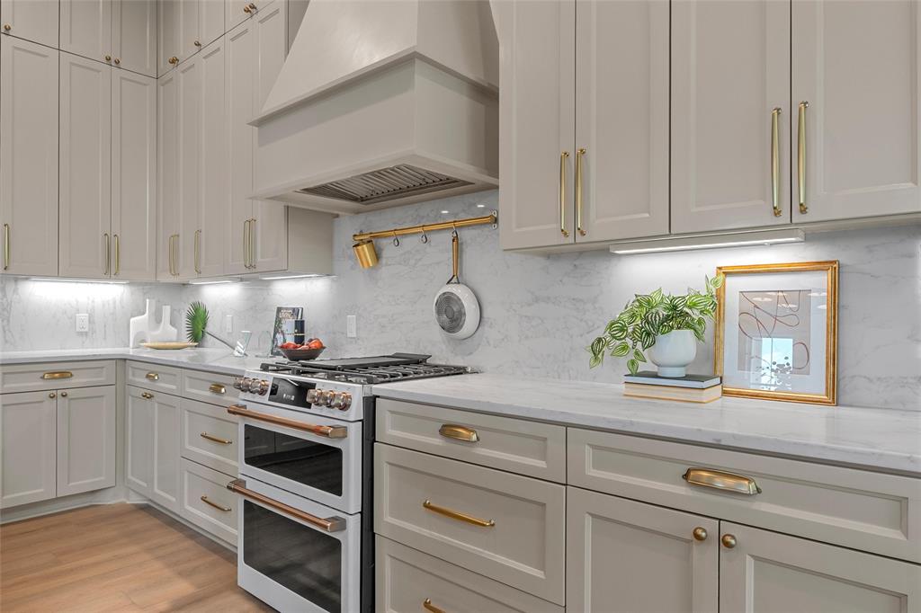 20 Ritchie Road Woodway, TX 76712 - Photo 10 of 40 Light-toned cabinetry with gold-toned hardware, stone countertops, stone backsplash, under-cabinet lighting, and a double oven range with a coordinating vent hood