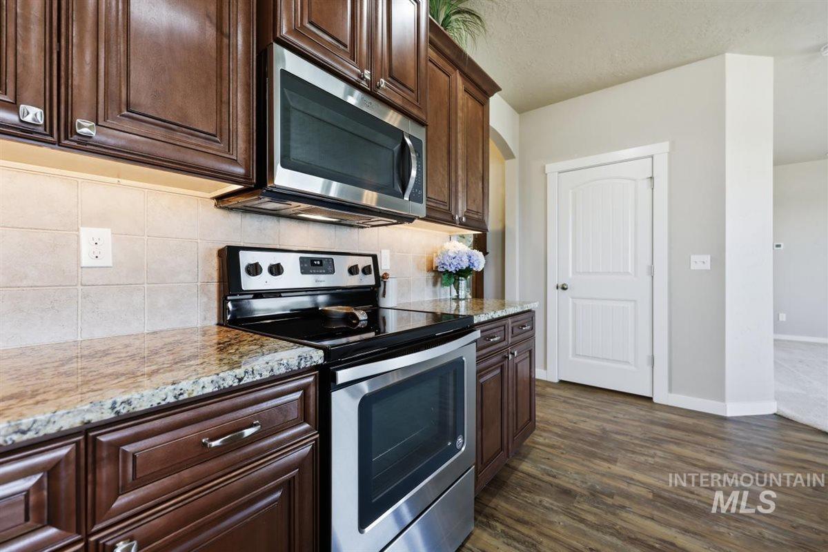 13496 Hockberger Ranch Road Caldwell, ID 83607 - Photo 16 of 40 Kitchen featuring wood-finish cabinetry with silver-tone hardware, stainless steel appliances, a tiled backsplash, and stone-look countertops