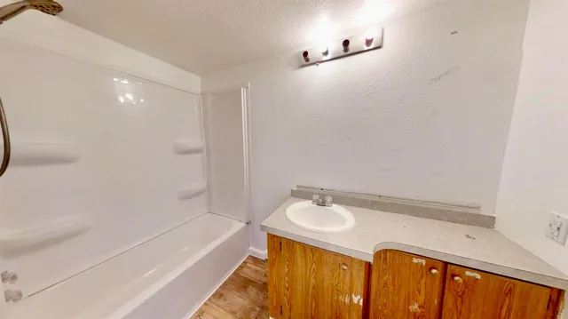 a view of a hallway with wooden floor and a bathroom