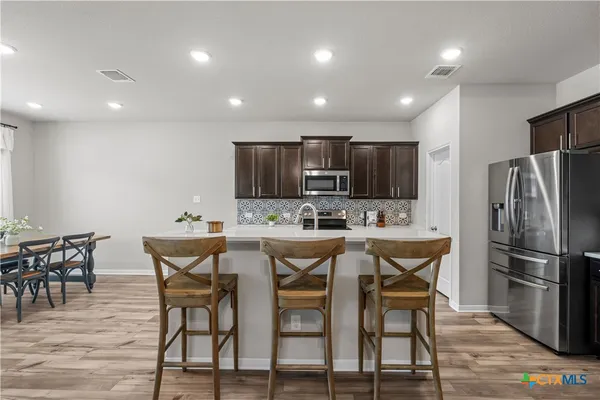 a kitchen with stainless steel appliances kitchen island granite countertop a dining table chairs refrigerator and microwave