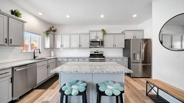 a kitchen with stainless steel appliances granite countertop a refrigerator a sink dishwasher a stove a dining table and chairs with wooden floor