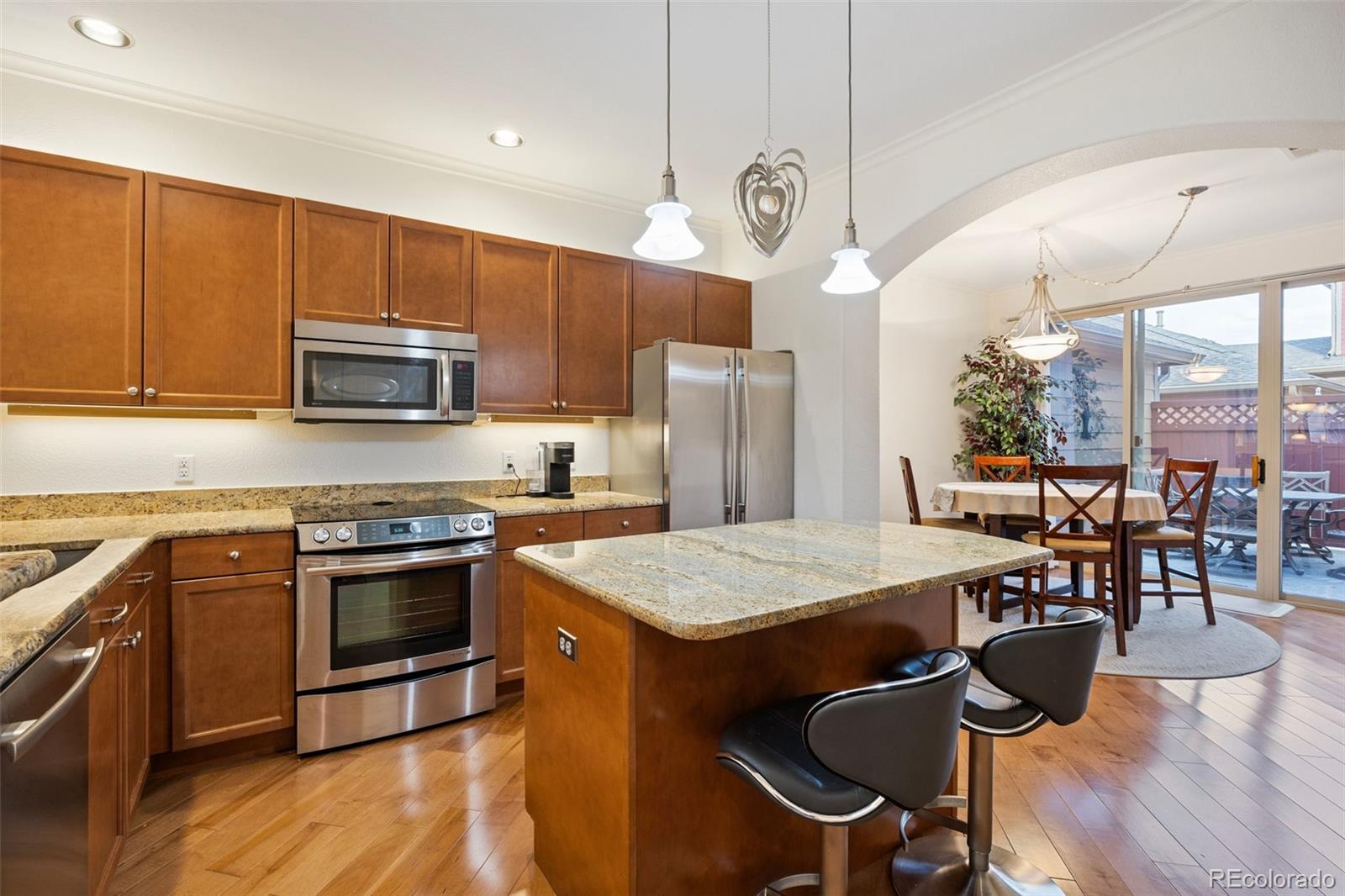 8558 Gold Peak Lane, Unit B Highlands Ranch, CO 80130 - Photo 2 of 41 a kitchen with stainless steel appliances granite countertop a stove a refrigerator a kitchen island a dining table and chairs with wooden floor