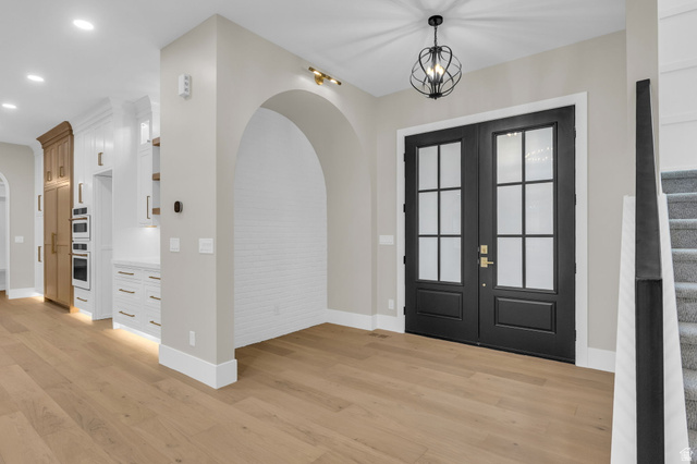 2828 Jojo Road Eagle Mountain, UT 84005 - Photo 6 of 63 Double black entry doors with frosted glass panels, an arched alcove with white brick-patterned wall, light wood-finish flooring, and a contemporary chandelier