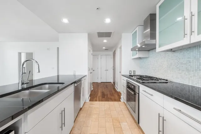 a large white kitchen with granite countertop a sink and dishwasher a stove top oven with wooden floor