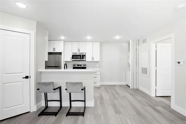 a kitchen with stainless steel appliances a refrigerator a stove top oven a sink and white walls with wooden floor