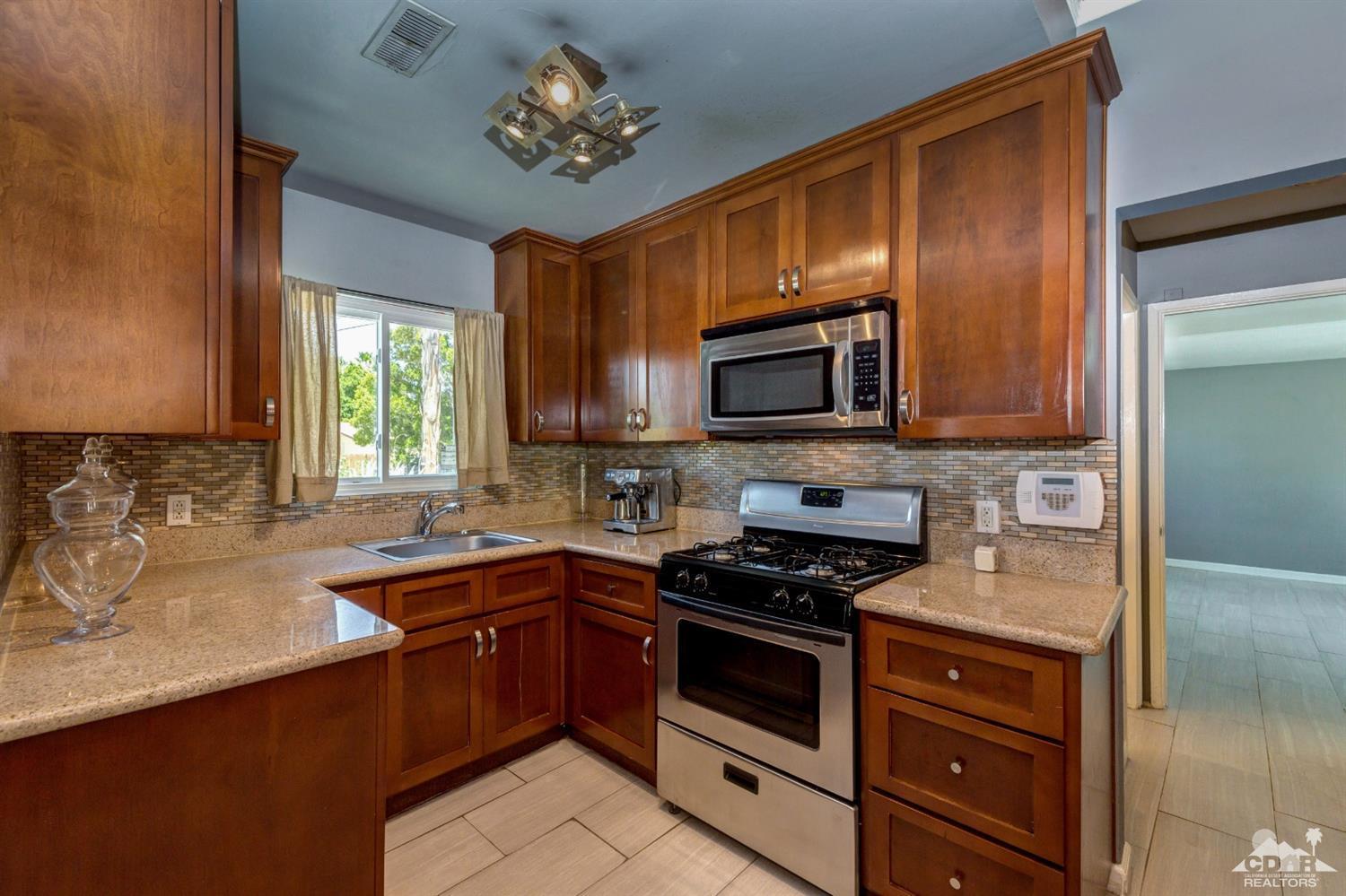 1950 North Magnolia Road Palm Springs, CA 92262 - Photo 12 of 36 a kitchen with stainless steel appliances granite countertop a sink dishwasher stove and microwave with wooden cabinets