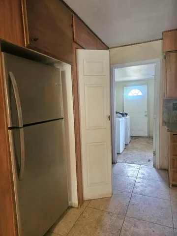 a view of a refrigerator in kitchen and an empty room in wooden floor