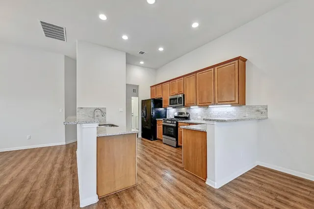 a kitchen with stainless steel appliances granite countertop wooden cabinets and a wooden floor