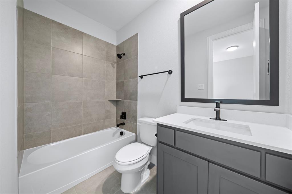 1173 Rochester Place Copper Canyon, TX 75077 - Photo 11 of 34 The bathroom features a white bathtub with tile surround, a toilet, and a vanity with a white countertop and a dark framed mirror