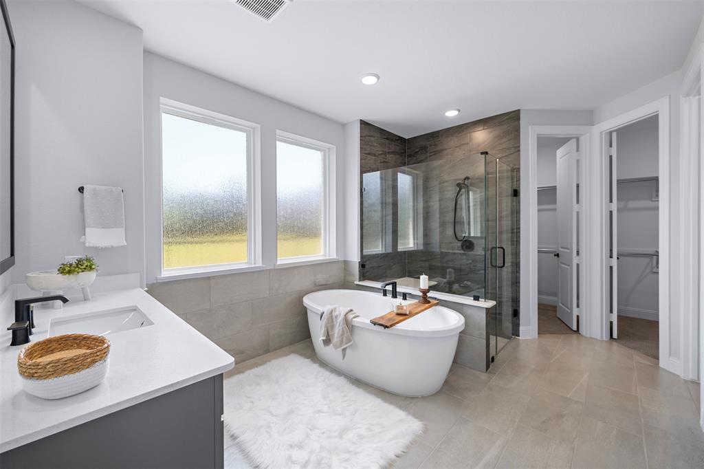 1173 Rochester Place Copper Canyon, TX 75077 - Photo 24 of 34 This bathroom features a freestanding bathtub, a walk-in shower with glass enclosure, a vanity with a white countertop and dark cabinetry, and tiled flooring