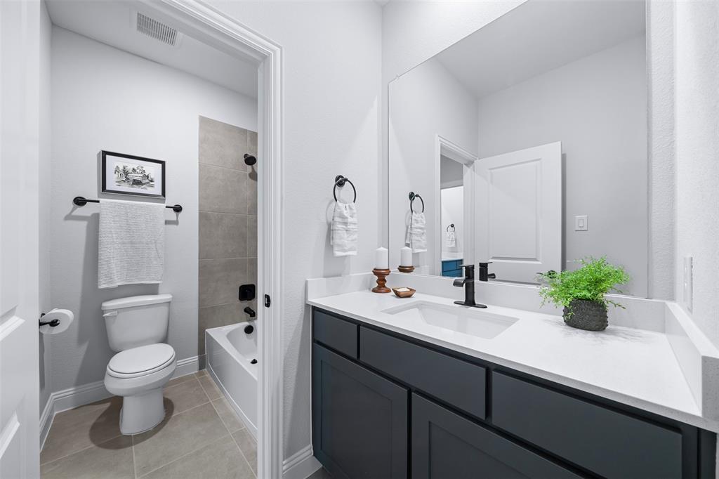1173 Rochester Place Copper Canyon, TX 75077 - Photo 27 of 34 This bathroom features a white vanity with a white countertop and a dark cabinet base, complemented by a large mirror and black fixtures