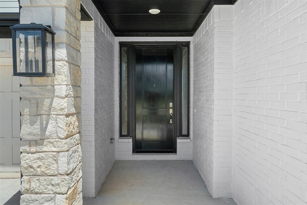 1173 Rochester Place Copper Canyon, TX 75077 - Photo 4 of 34 Entryway featuring a dark paneled door with sidelights, white brick walls, and a stone pillar with an exterior light fixture