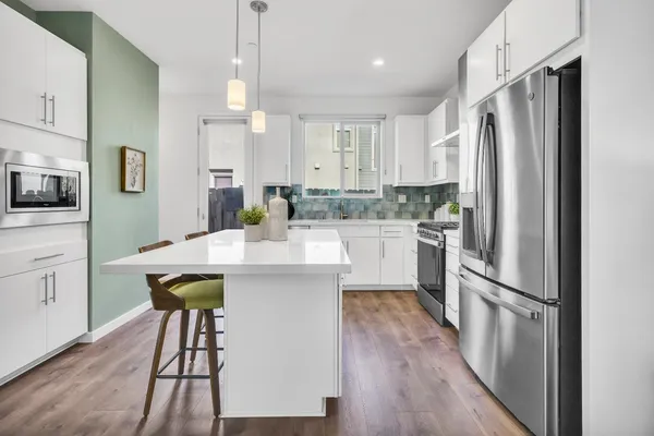 a kitchen with stainless steel appliances a dining table chairs refrigerator and microwave