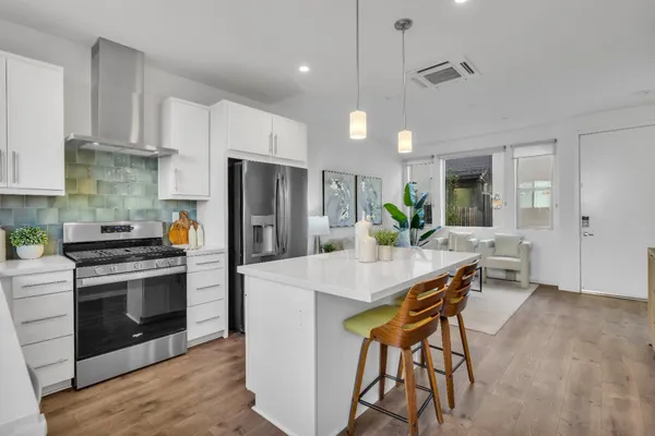 a kitchen with stainless steel appliances kitchen island a stove a refrigerator a sink dishwasher a dining table and chairs with wooden floor