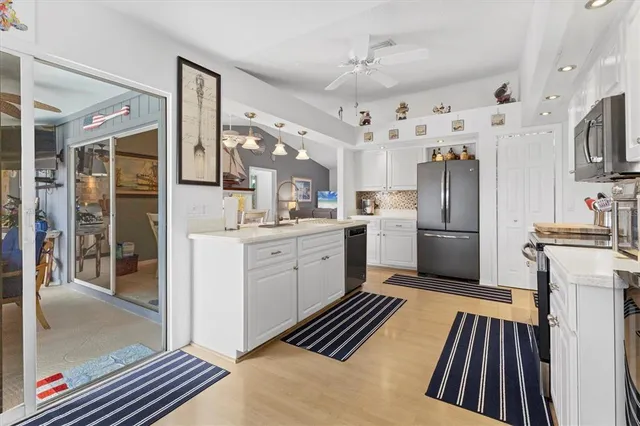 a kitchen with stainless steel appliances kitchen island granite countertop a refrigerator a stove a sink dishwasher and white cabinets with wooden floor