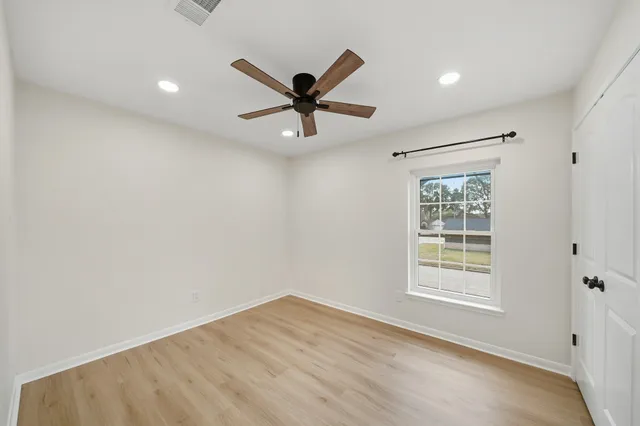 an empty room with wooden floor ceiling fan and windows