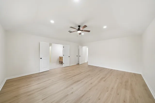 an empty room with wooden floor chandelier fan and windows