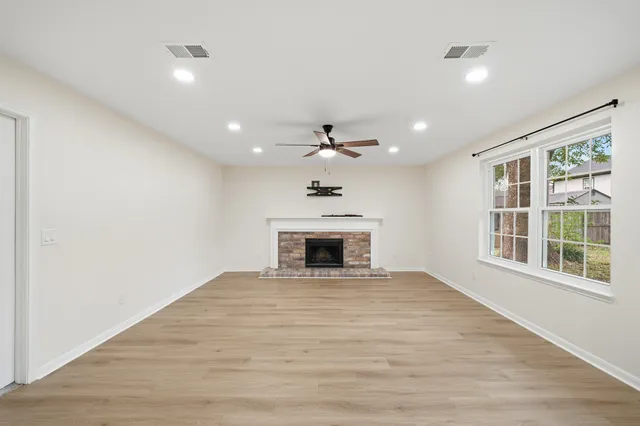 a view of an empty room with wooden floor fireplace and a window