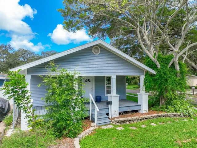 a view of a house with a yard potted plants and a large tree