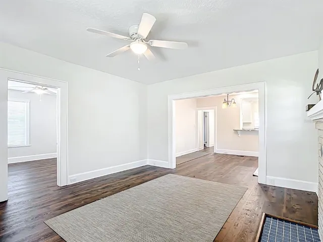an empty room with wooden floor fan and windows