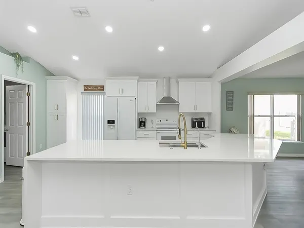 a large white kitchen with kitchen island a sink stainless steel appliances and cabinets