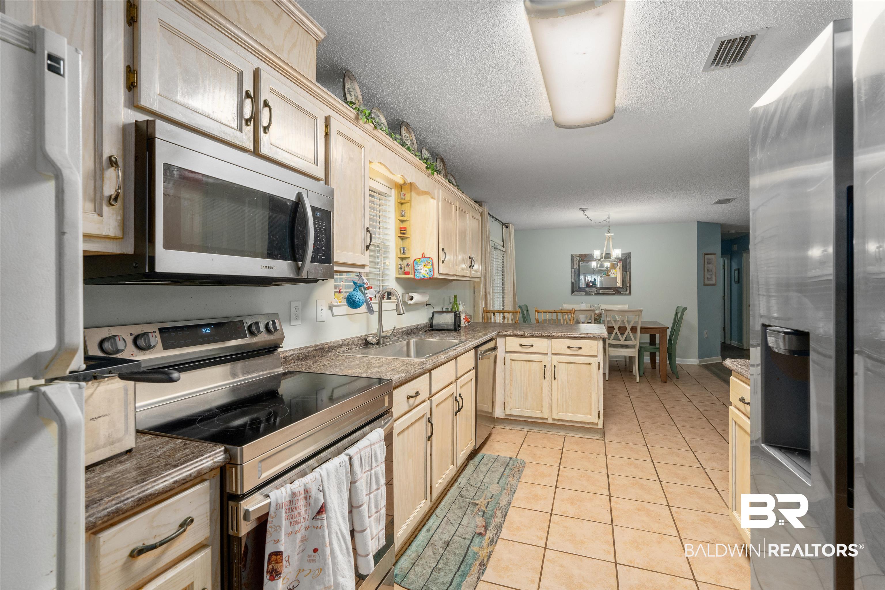 23186 Pecan Street Robertsdale, AL 36567 - Photo 5 of 36 Kitchen with appliances with stainless steel finishes, light brown cabinetry, light tile patterned flooring, a textured ceiling, and decorative light fixtures