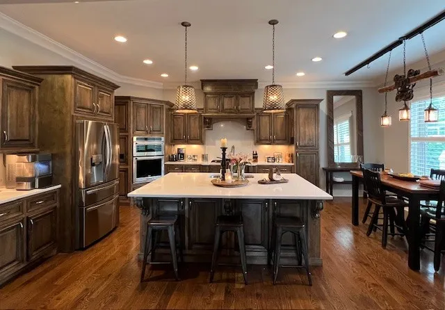 a kitchen with stainless steel appliances kitchen island granite countertop a dining table chairs and wooden floor