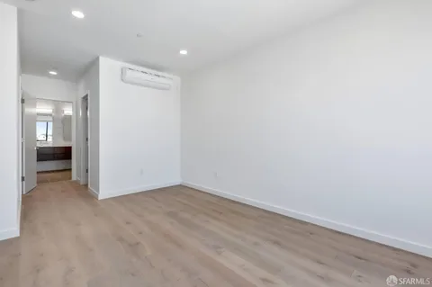 a view of an empty room with wooden floor and a kitchen