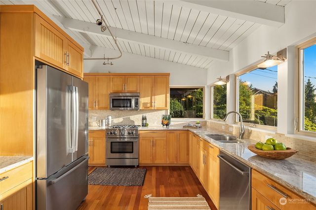 a kitchen with stainless steel appliances granite countertop a refrigerator a sink dishwasher a stove and a dining table with wooden floor