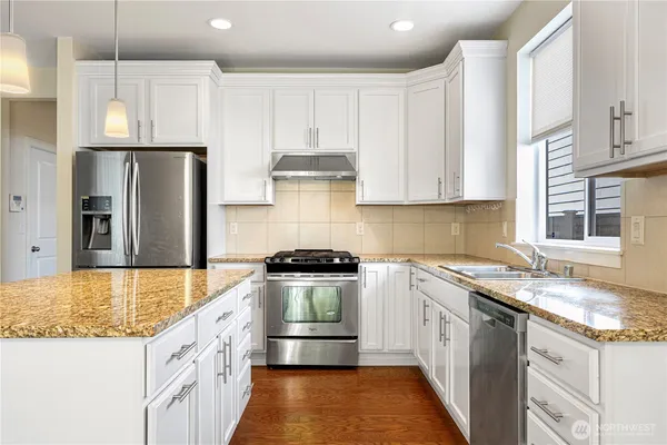 a large kitchen with a large center island wooden floor stainless steel appliances and cabinets